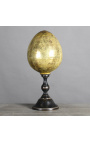 Duże żółte jajko z dmuchanego szkła na czarnej rzeźbionej drewnianej podstawie