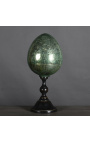 Suuri vihreä muna puhalletussa lasissa mustalla veistetyllä puupohjalla