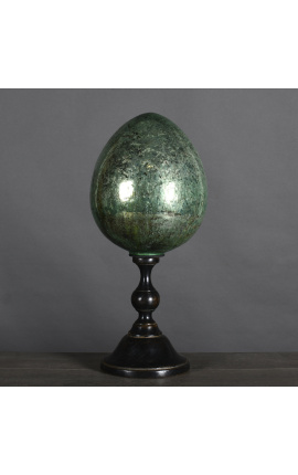 Duże zielone jajko z dmuchanego szkła na czarnej rzeźbionej drewnianej podstawie