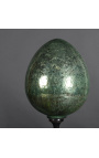 Duże zielone jajko z dmuchanego szkła na czarnej rzeźbionej drewnianej podstawie